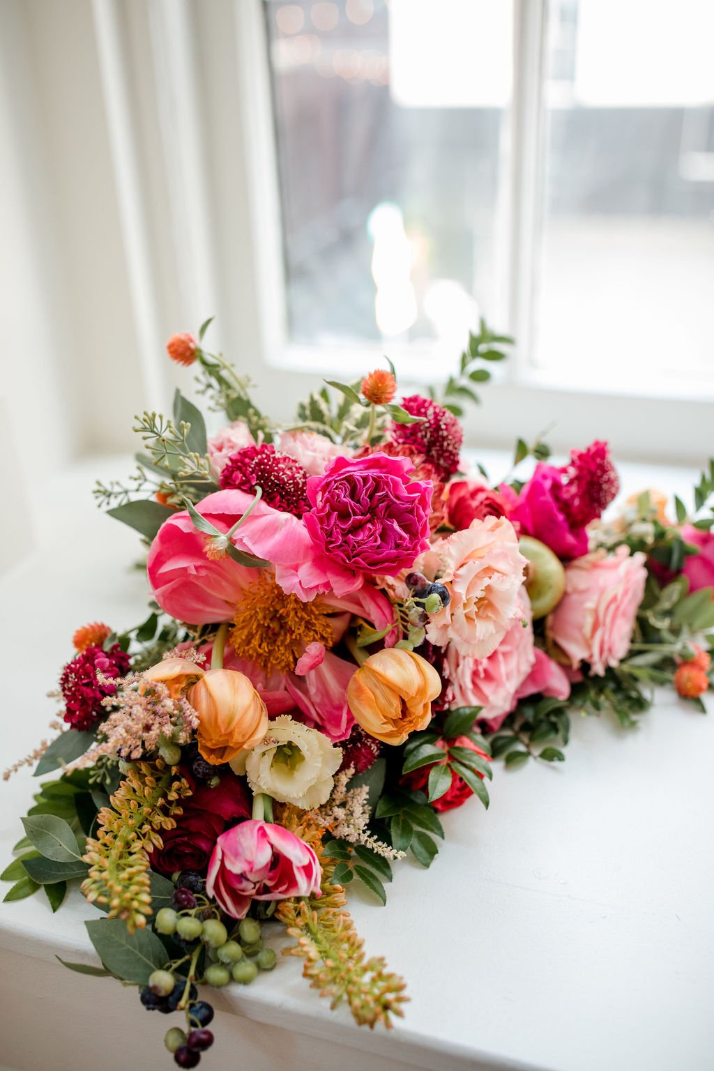 Lush and artful bridal bouquet with textural accents. Balanced color palette of pinks, oranges and muted burgundy tones featuring garden roses, peonies, ranunculus and tulips. Nashville wedding florist at Hotel Noelle.