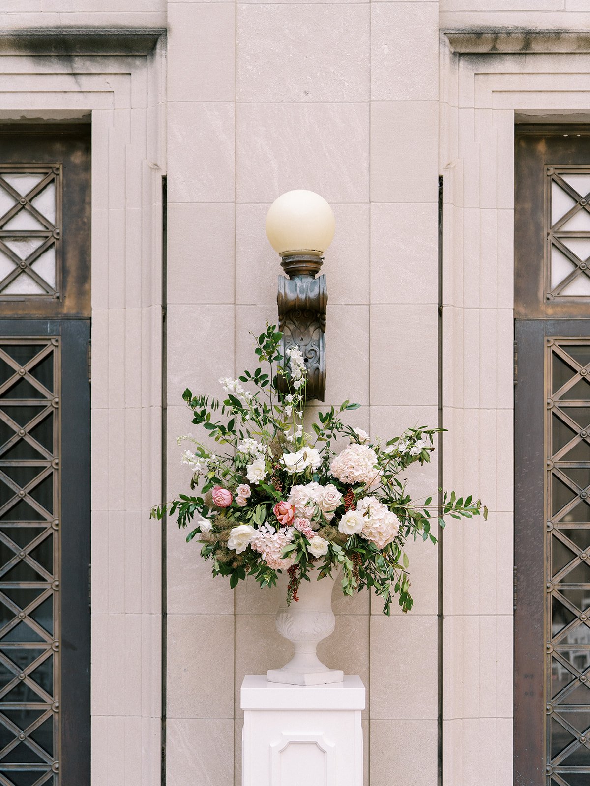 A ceremony backdrop comprised of marble urns filled with overflowing greenery, hydrangea, garden roses, spray roses, and pepper berry. Floral Design by Rosemary and Finch in Nashville, TN.