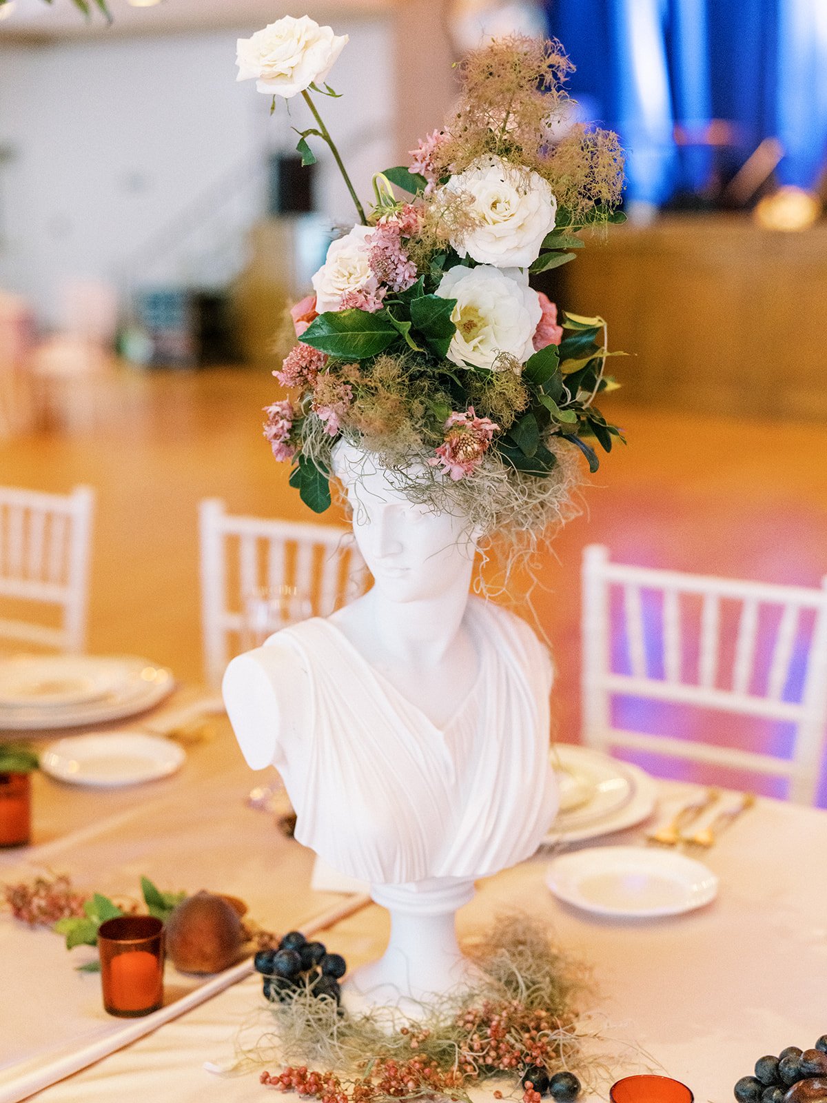 Beautiful reception adorned with marble busts covered in florals and lush centerpieces. The summer solstice color palette was filled with garden roses, peonies, ranunculus, pepper berry and fresh fruit. Design by Rosemary and Finch in Nashville, TN.