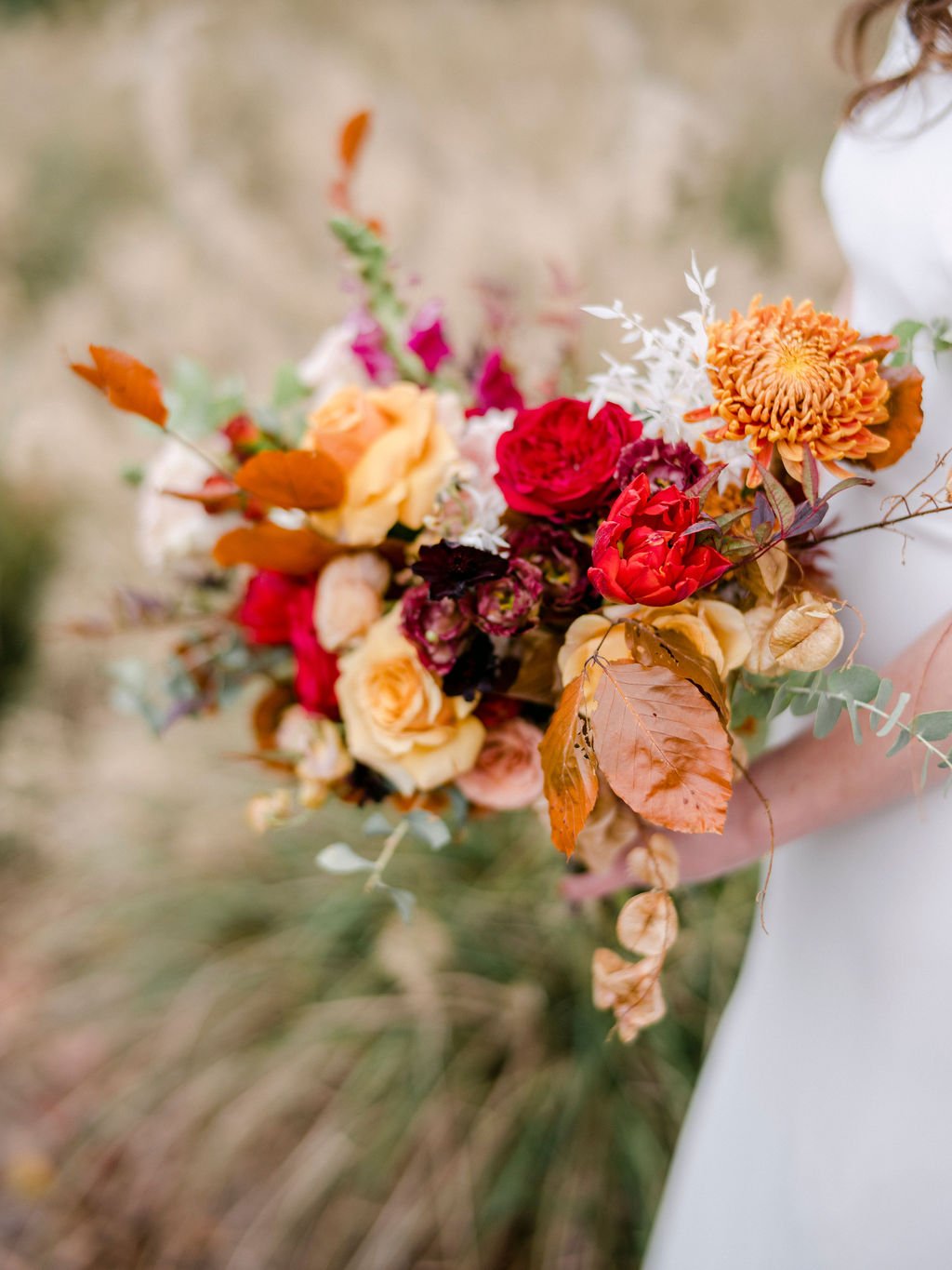 An elegant bridal bouquet filled with vibrant red, cream, terra cotta, and burnt orange florals. The bouquet features roses, tulips, carnations, eucalyptus, and dried floral accents. Design by Rosemary and Finch in Nashville, TN. Location Atlanta, GA