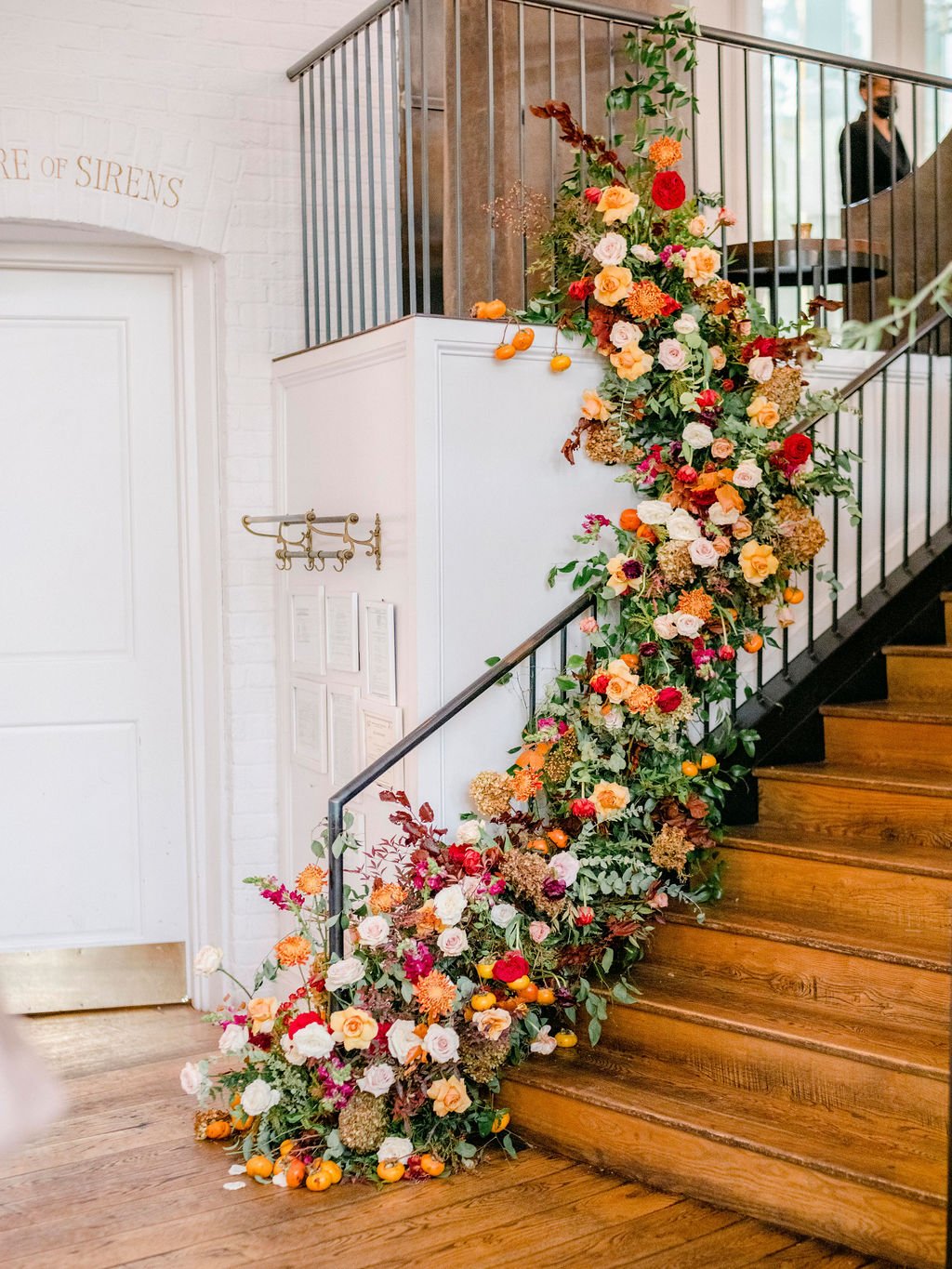 Gorgeous cascading staircase floral installation of fall foliage, lush greenery, and florals inviting guests into the reception space. Located in The St. Cecilia restaurant in Atlanta, GA. Floral Design by Rosemary and Finch in Nashville, TN.