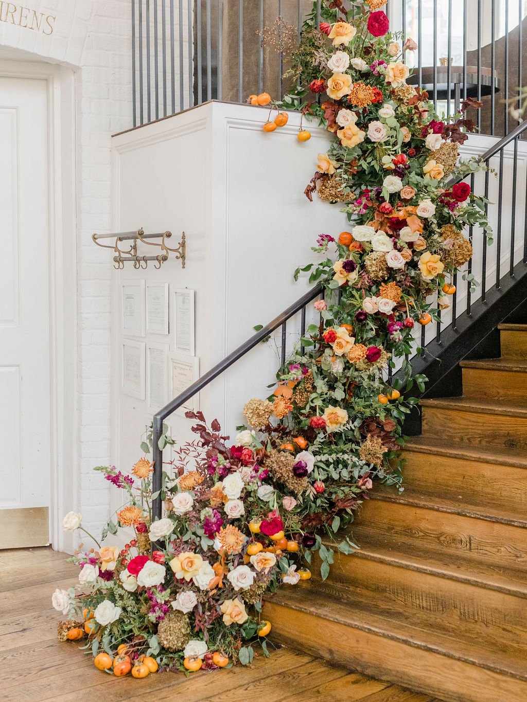 Gorgeous cascading staircase floral installation of fall foliage, lush greenery, and florals inviting guests into the reception space. Located in The St. Cecilia restaurant in Atlanta, GA. Floral Design by Rosemary and Finch in Nashville, TN.