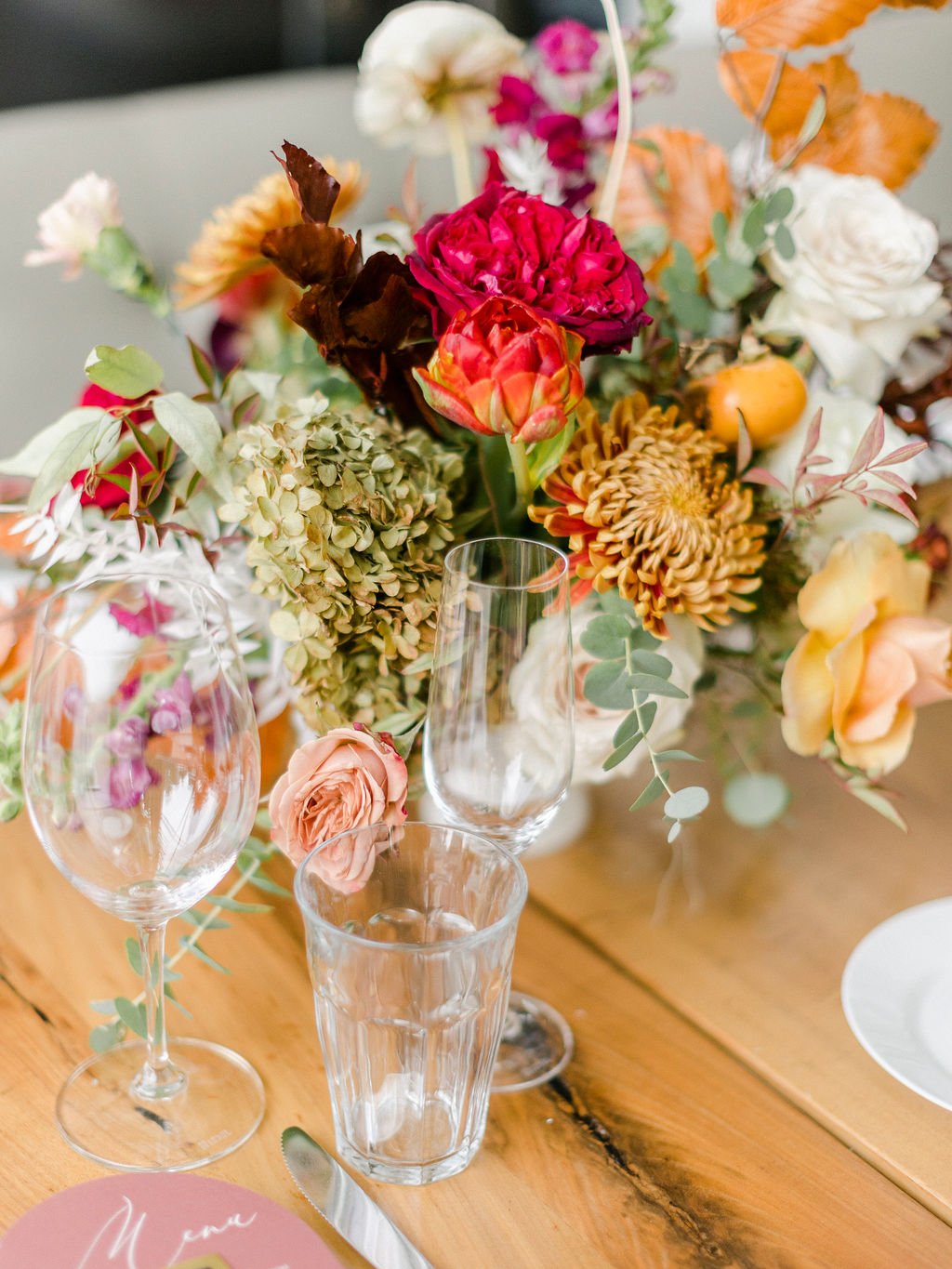 Eye-catching floral centerpieces comprised of tangerine, dusty rose, terra cotta, and deep red florals. Featuring garden roses, dried foliage, and fruity persimmons branches. Floral design by Rosemary and Finch in Nashville, TN.