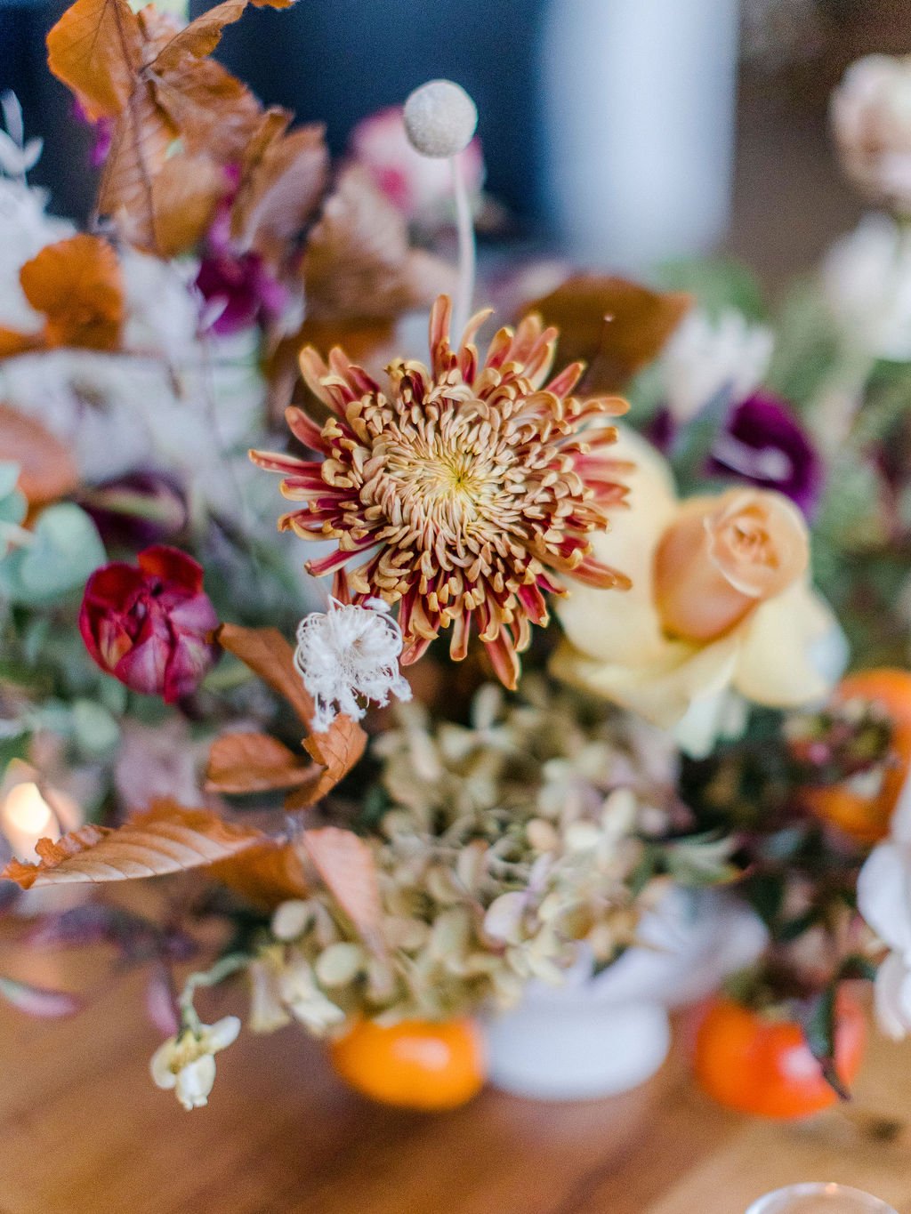 Eye-catching floral centerpieces comprised of tangerine, dusty rose, terra cotta, and deep red florals. Featuring garden roses, dried foliage, and fruity persimmons branches. Floral design by Rosemary and Finch in Nashville, TN.