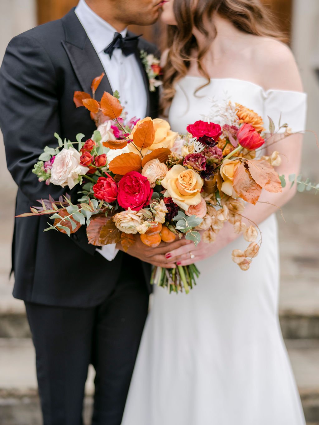 An elegant fall bridal bouquet filled with vibrant red, cream, terra cotta, and burnt orange florals. The bouquet features roses, tulips, carnations, eucalyptus, and dried floral accents. Design by Rosemary and Finch in Nashville, TN.