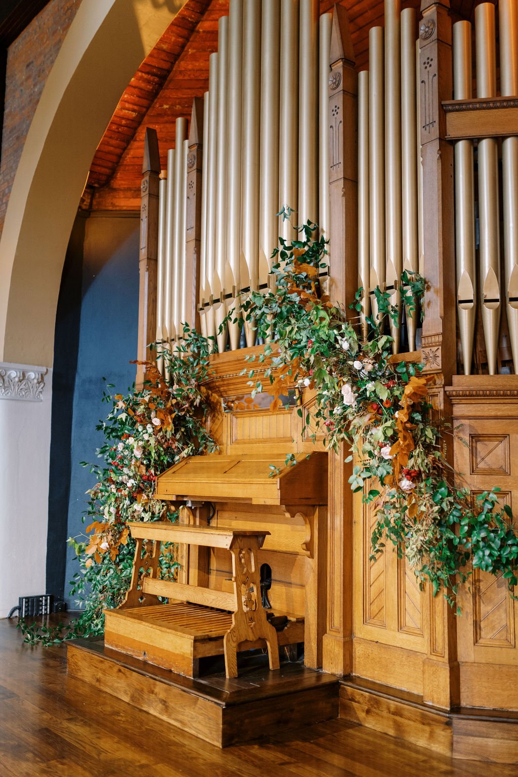 Lush and whimsical asymmetrical installation highlighting the organ was filled with greenery, autumnal foliage, and garden roses. Floral Design by Rosemary and Finch in Nashville, TN.