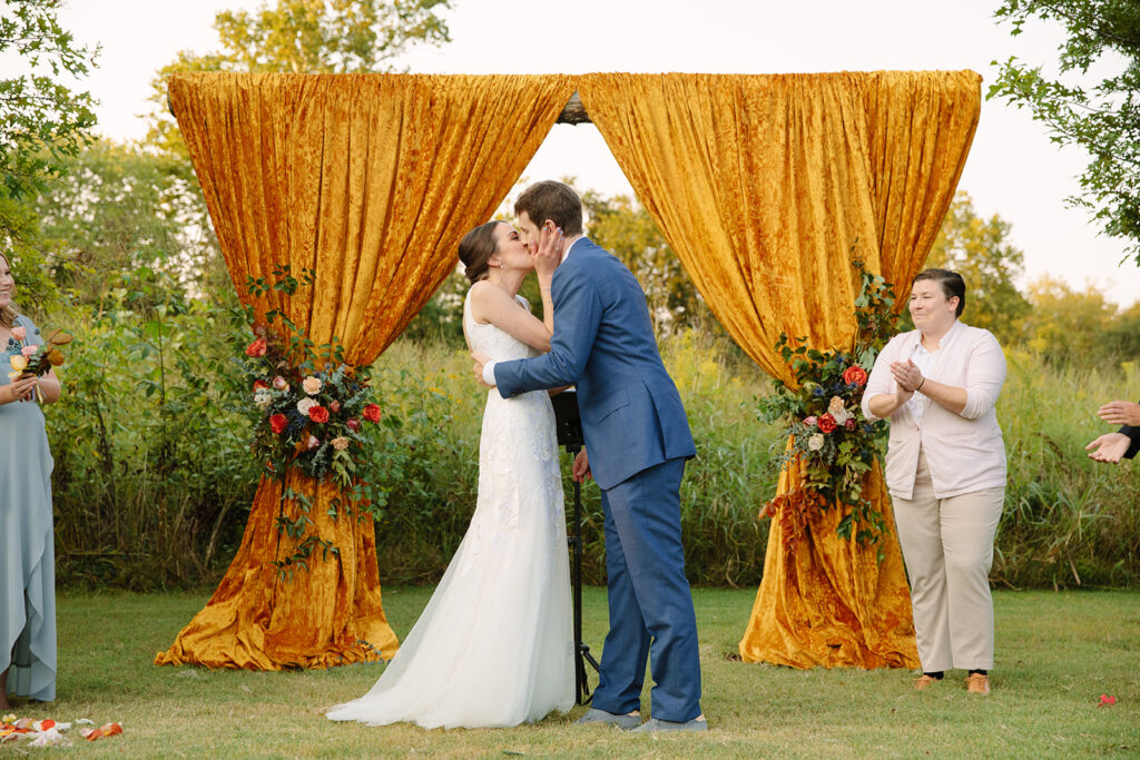 Gorgeous ceremony floral installation accenting vibrant yellow drapery. Featuring roses in hues of deep orange, dusty rose, and terra cotta. Designed by Rosemary and Finch in Nashville, TN.