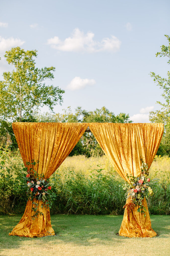Gorgeous ceremony floral installation accenting vibrant yellow drapery. Featuring roses in hues of deep orange, dusty rose, and terra cotta. Designed by Rosemary and Finch in Nashville, TN.