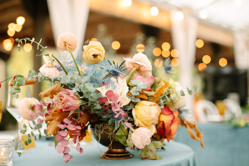 Beautiful fall centerpieces with hues of mustard yellow, terra cotta, sage green, dusty blue, and blush to the reception space. Bright florals include ranunculus, thistle, roses, and foliage. Designed by Rosemary and Finch in Nashville, TN.