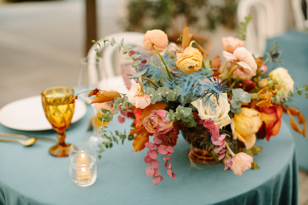 Beautiful fall centerpieces with hues of mustard yellow, terra cotta, sage green, dusty blue, and blush to the reception space. Bright florals include ranunculus, thistle, roses, and foliage. Designed by Rosemary and Finch in Nashville, TN.