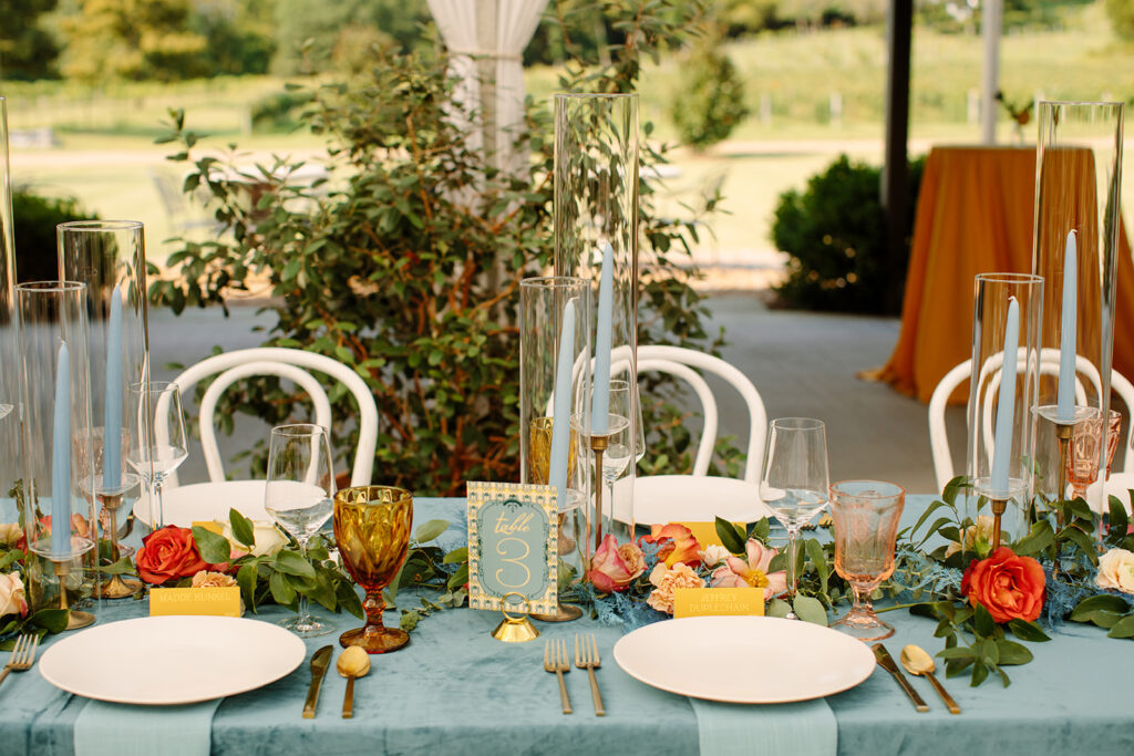 Warm fall table settings with hues of mustard yellow, terra cotta, sage green, dusty blue, and blush to the reception space. Bright florals include ranunculus, thistle, roses, and foliage. Designed by Rosemary and Finch in Nashville, TN.