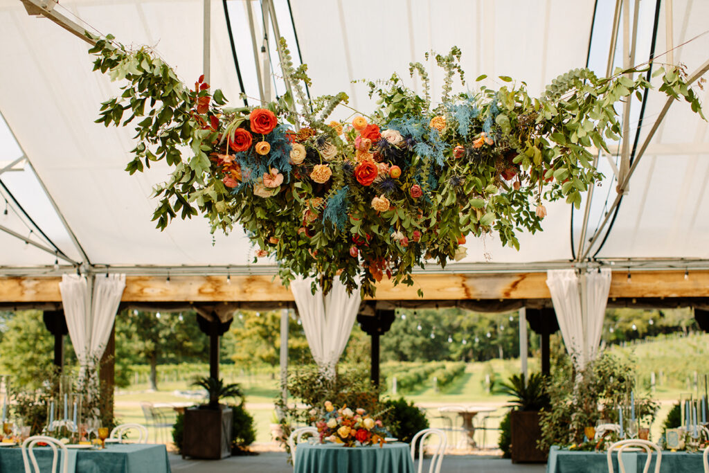 Eye-Catching wedding floral installation featuring petal heavy roses, ranunculus, dusty blue thistle, eucalyptus, and fall foliage. Lush design complemented by hues of mustard yellow, terra cotta, sage green, and dusty rose. Designed by Rosemary and Finch in Nashville, TN.