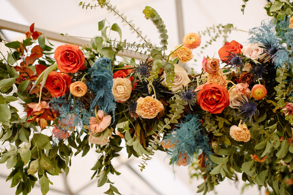 Eye-Catching wedding floral installation featuring petal heavy roses, ranunculus, dusty blue thistle, eucalyptus, and fall foliage. Lush design complemented by hues of mustard yellow, terra cotta, sage green, and dusty rose. Designed by Rosemary and Finch in Nashville, TN.