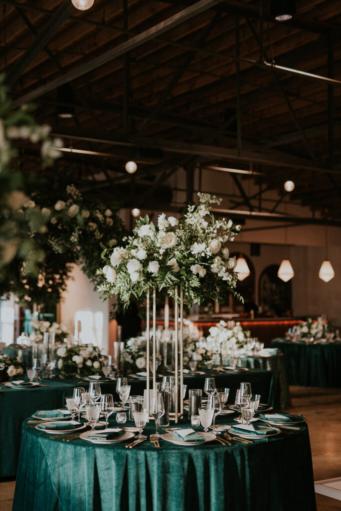 Elevated gold stands with lush floral centerpieces of white garden roses, ranunculus, delphinium, waxflower, lisianthus, carnations, and natural greenery. Floral hues of white, cream, black, and emerald. Designed by Rosemary and Finch in Nashville, TN.
