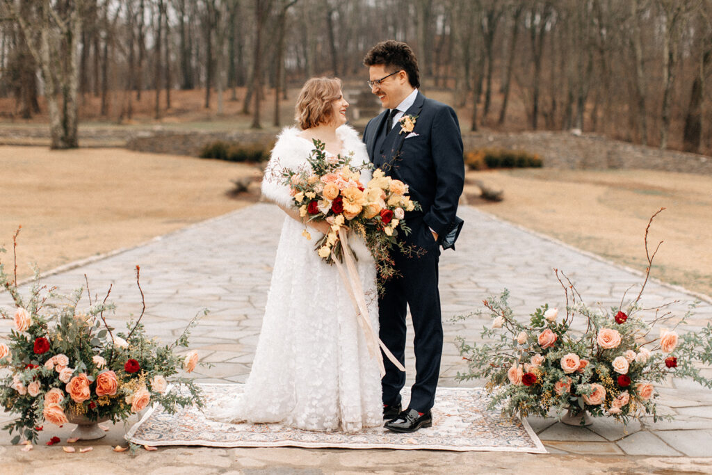 Organic growing wedding ceremony urns in floral hues of dusty pink, red, pale yellow, and sage green composed of petal heavy roses, garden roses, eucalyptus, winter branches, and natural greenery. Design by Rosemary and Finch in Nashville, TN. 