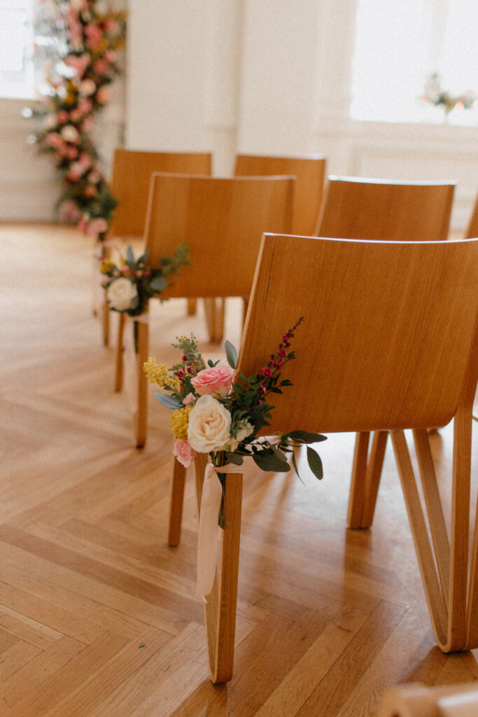 Delicate aisle markers hang on the chairs of this winter downtown wedding composed of petal heavy roses, blooming branches, spray roses, acacia, and eucalyptus creating hues of pink, mustard yellow, burgundy, white, and sage green. Design by Rosemary and Finch in Nashville, TN.