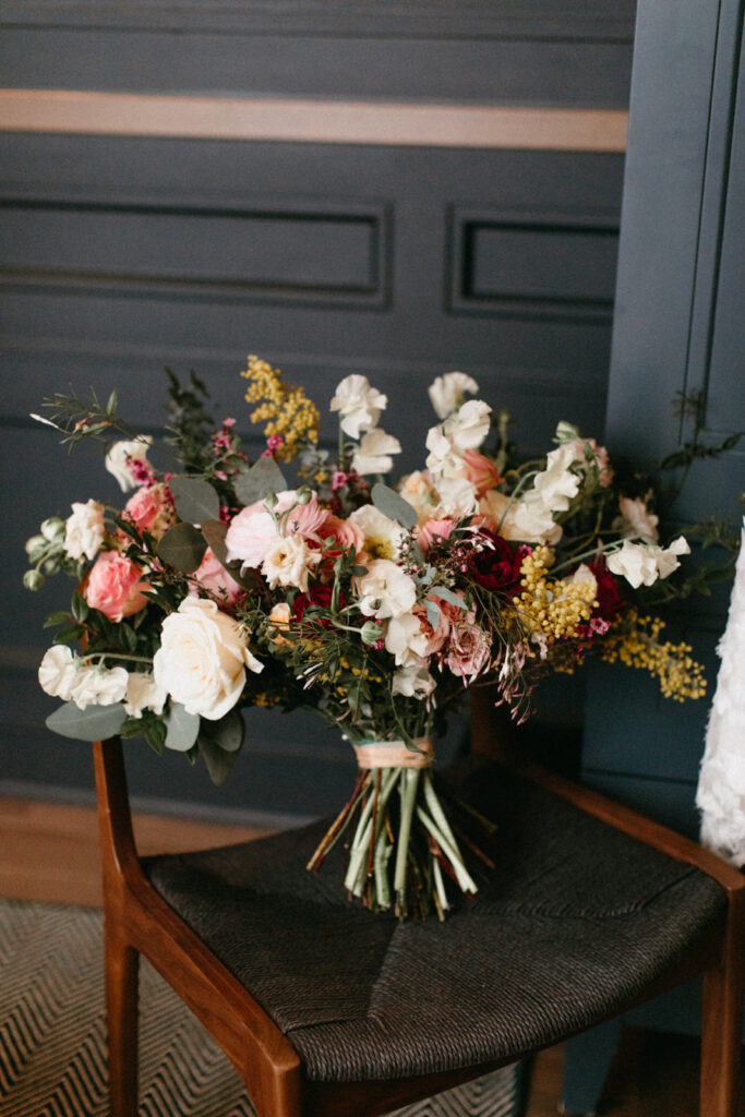 Lush winter bridal bouquet in floral hues of white, burgundy, mustard yellow, pink, and sage green composed of roses, sweet peas, spray roses, acacia, butterfly ranunculus, and eucalyptus. Design by Rosemary and Finch in Nashville, TN. 