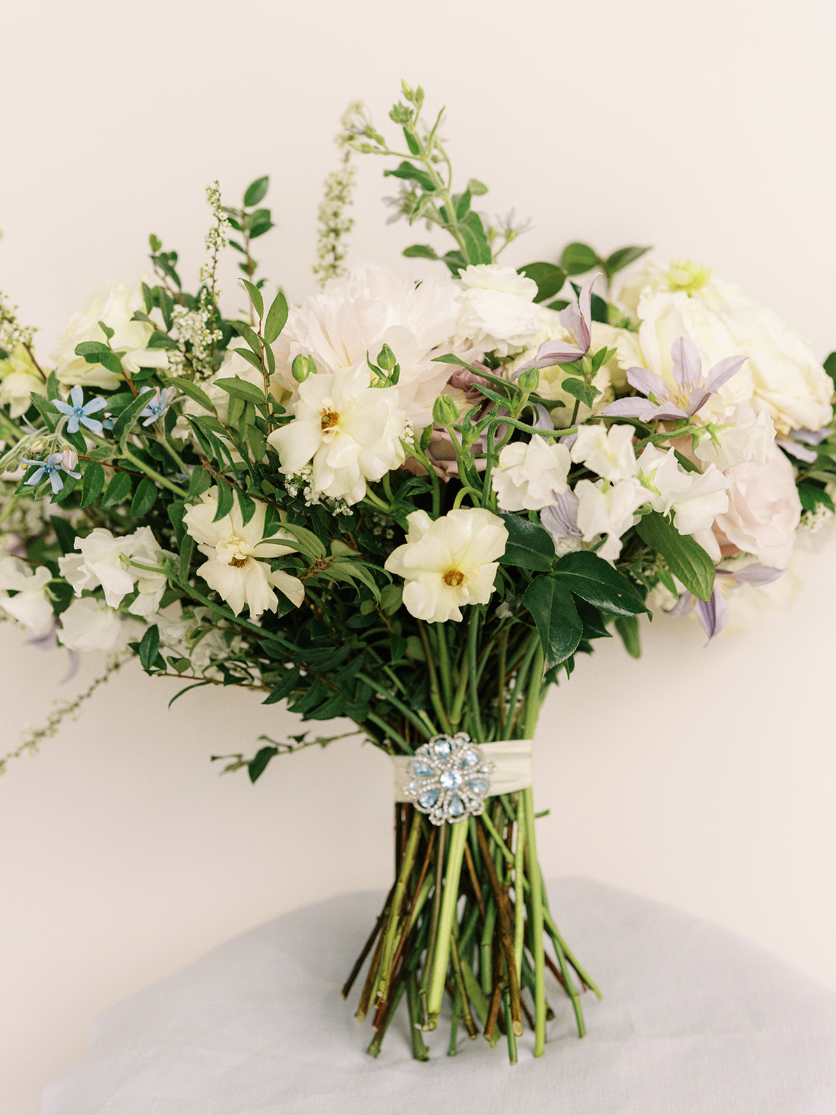 Classic white, green, and lavender garden inspired bridal bouquet with peonies, roses, clematis, spirea, butterfly ranunculus, and ranunculus florals. Spring church wedding large lush bridal bouquet. Design by Rosemary and Finch Floral Design in Nashville, TN.