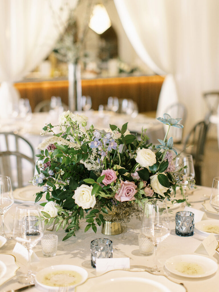 Lush garden-spired spring wedding reception table centerpieces featuring colors of cream, white, mauve, lavender, and green. Including roses, butterfly ranunculus, tulips, spirea, clematis, and greenery. Design by Rosemary and Finch Floral Design in downtown Nashville, TN.