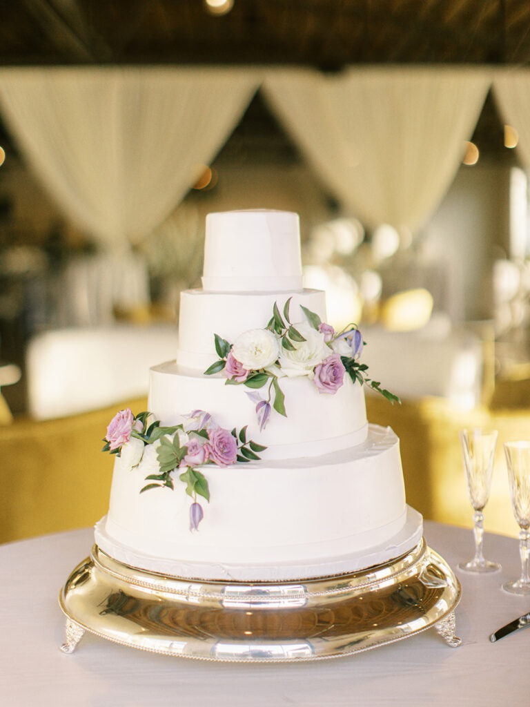 Elegant cake flowers add color to this all white classic wedding cake. Flower colors in pink, purple, lavender, white, cream, and green featuring roses, ranunculus, and greenery. Design by Rosemary and Finch Floral Design in Nashville, TN.