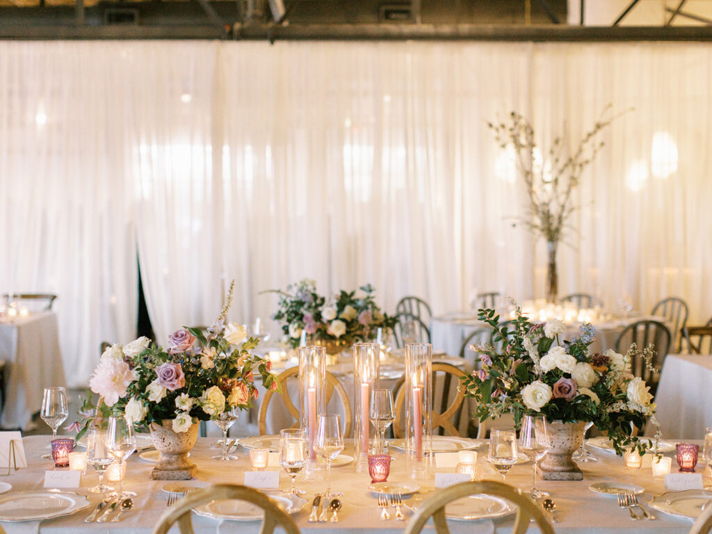 Lush garden-spired spring wedding reception table centerpieces featuring colors of cream, white, mauve, lavender, and green. Including roses, butterfly ranunculus, tulips, spirea, clematis, and greenery. Design by Rosemary and Finch Floral Design in downtown Nashville, TN.