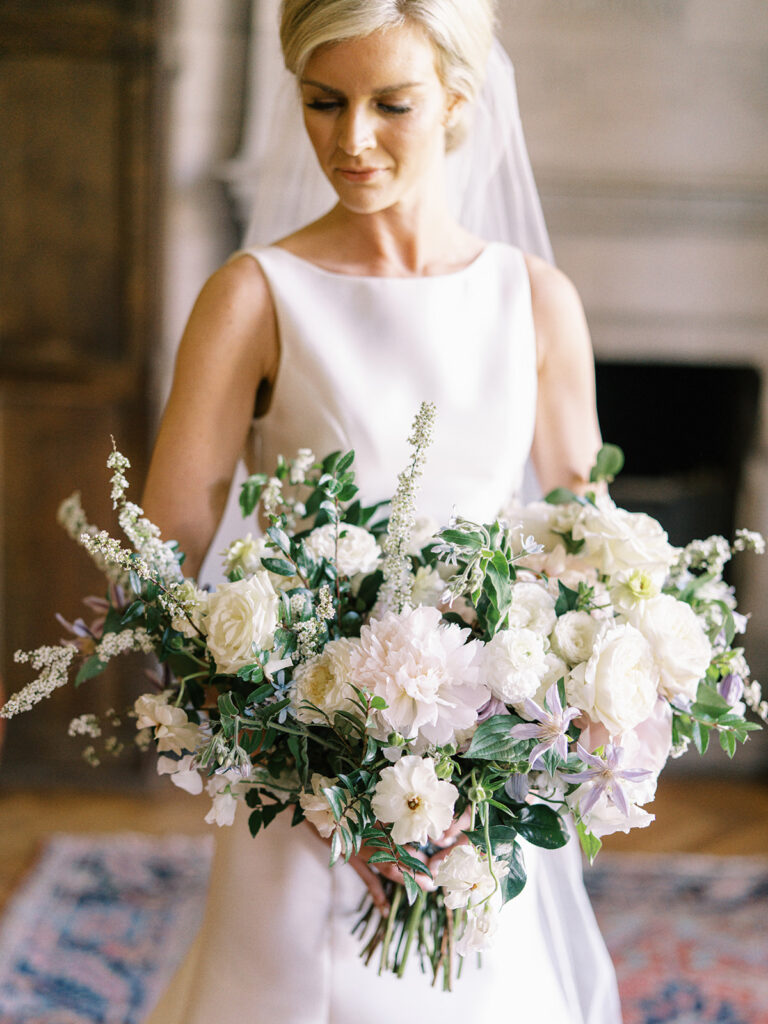Classic white, green, and lavender garden inspired bridal bouquet with peonies, roses, clematis, spirea, butterfly ranunculus, and ranunculus florals. Spring church wedding large lush bridal bouquet. Design by Rosemary and Finch Floral Design in Nashville, TN.