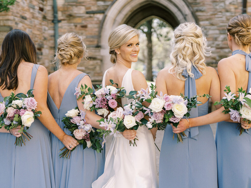 Classic white, green, and lavender garden inspired bridal party bridesmaid’s bouquets with peonies, roses, clematis, spirea, butterfly ranunculus, and ranunculus florals. Spring church wedding large lush bridal bouquet. Design by Rosemary and Finch Floral Design in Nashville, TN.