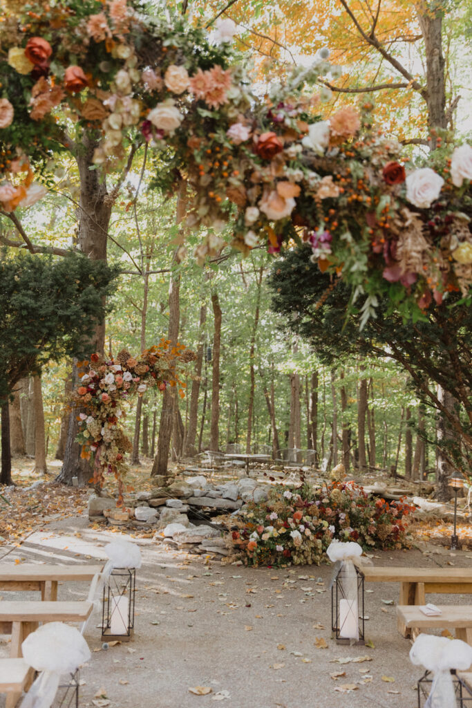 Asymmetrical hanging and growing fall wedding ceremony floral installation in colors of burgundy, plum, copper, pale yellow, terra cotta, cream, dusty pink, and lavender. Hanging flowers over intimate fall wedding ceremony aisle. Design by Rosemary and Finch Floral Design in Nashville, TN.