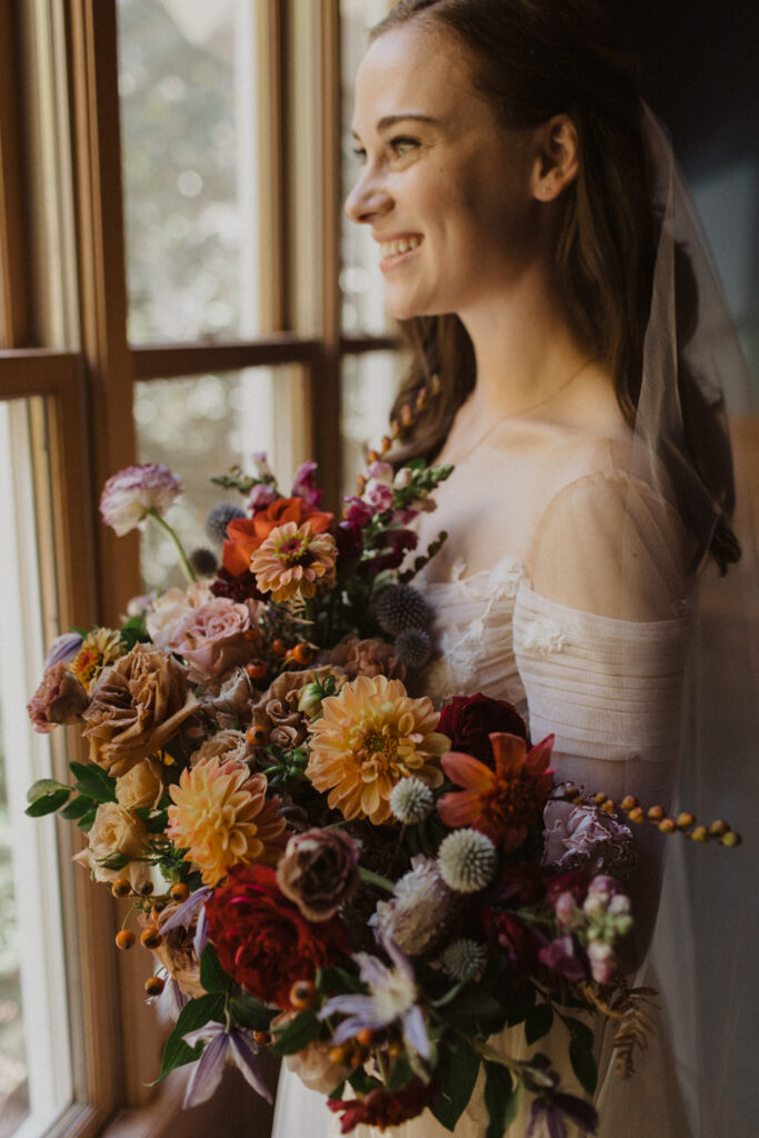 Lush fall vibrant bridal bouquet in flower colors of burgundy, peach, red, lavender, plum, terra cotta, dusty blue, and pale yellow. Abundance of fall colors and fall flowers for bride’s bouquet. Intimate fall wedding on private property in Nashville, TN. Design by Rosemary and Finch Floral Design in Nashville, TN. 