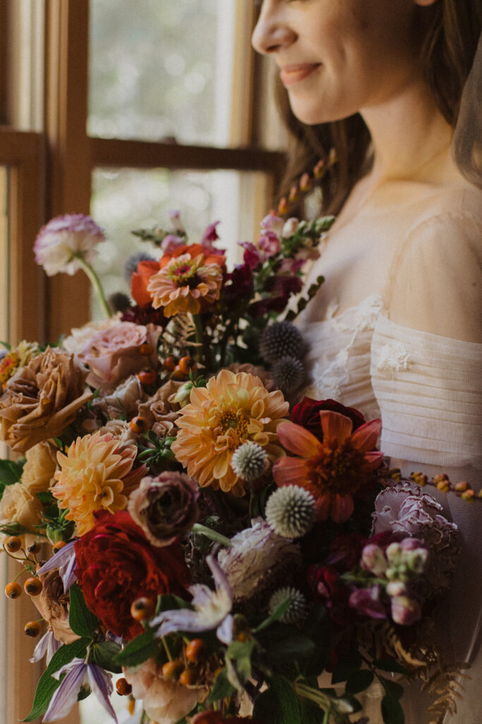 Lush fall vibrant bridal bouquet in flower colors of burgundy, peach, red, lavender, plum, terra cotta, dusty blue, and pale yellow. Abundance of fall colors and fall flowers for bride’s bouquet. Intimate fall wedding on private property in Nashville, TN. Design by Rosemary and Finch Floral Design in Nashville, TN. 