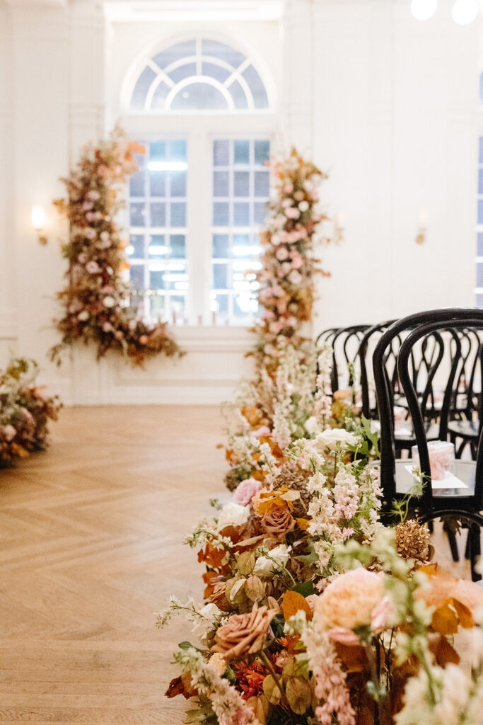 Lush aisle hedges line the entryway for this autumnal wedding with florals composed of roses, clematis, mums, delphinium, copper beech, and fall foliage creating hues of burgundy, dusty rose, copper, mauve, taupe, and lavender. Fall wedding in Downtown Nashville. Design by Rosemary & Finch Floral Design in Nashville, TN. 