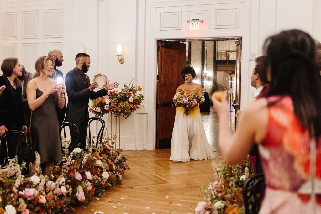 Lush aisle hedges line the entryway for this autumnal wedding with florals composed of roses, clematis, mums, delphinium, copper beech, and fall foliage creating hues of burgundy, dusty rose, copper, mauve, taupe, and lavender. Fall wedding in Downtown Nashville. Design by Rosemary & Finch Floral Design in Nashville, TN. 