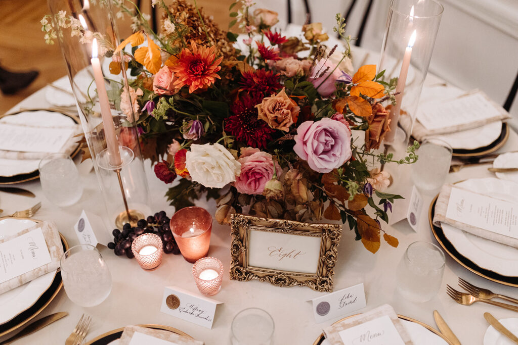 Organic fall floral centerpieces decorate this autumnal Parisian inspired wedding reception in hues of dusty rose, burgundy, terra cotta, and lavender composed of roses, ranunculus, delphinium, lisianthus, copper beech, and fall foliage. Fall wedding in Downtown Nashville. Design by Rosemary & Finch Floral Design in Nashville, TN. 