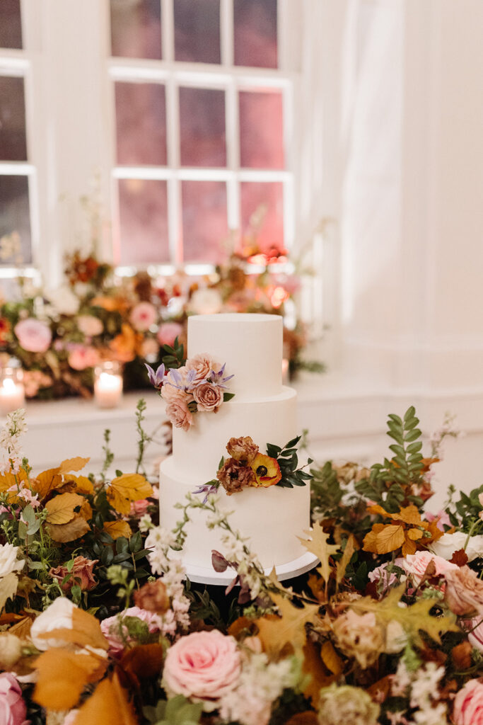 Lush floral meadows surround the wedding cake at this Parisian inspired fall wedding with colors of dusty rose, terra cotta, mauve, copper, and lavender composed of roses, ranunculus, copper beech, clematis, and fall foliage. Fall Wedding in Downtown Nashville. Design by Rosemary & Finch Floral Design in Nashville, TN. 