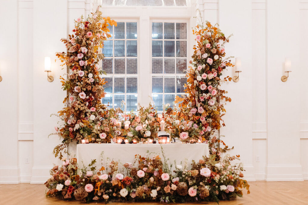 Artful asymmetrical floral fall wedding ceremony backdrop sets the autumnal colors of mauve, dusty rose, burgundy, terra cotta, and copper florals composed of roses, copper beech, delphinium, raintree pods, mums, and fall foliage. Fall wedding in Downtown Nashville. Design by Rosemary & Finch Floral Design in Nashville, TN. 