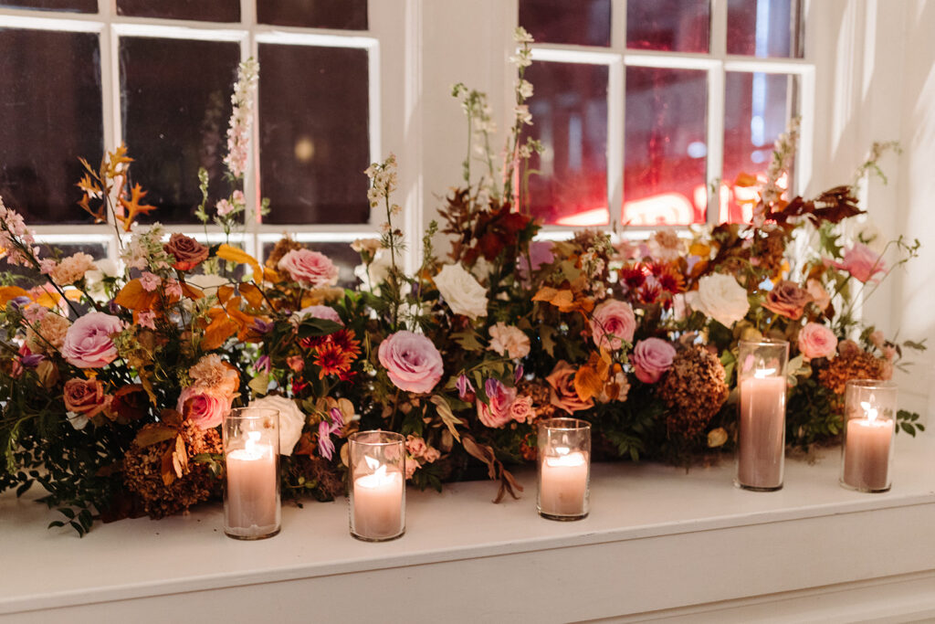 Elegant window arrangements and candle moments create a warm autumnal setting in hues of dusty rose, burgundy, taupe, mauve, and lavender florals composed of roses, raintree pods, ranunculus, spray roses, copper beech, and fall foliage. Fall wedding in Downtown Nashville. Design by Rosemary & Finch Floral Design in Nashville, TN. 