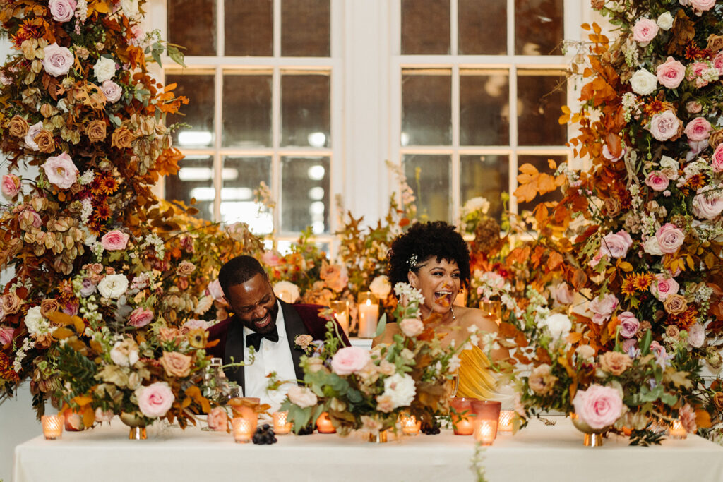 Lush growing fall floral installation surrounds the couple at this autumnal wedding’s sweetheart table composed of roses, ranunculus, lisianthus, dried hydrangea, delphinium, copper beech, and fall foliage creating floral colors of dusty rose, burgundy, mauve, copper, terra cotta, and hints of lavender. Fall wedding in Downtown Nashville. Design by Rosemary & Finch Floral Design in Nashville, TN. 