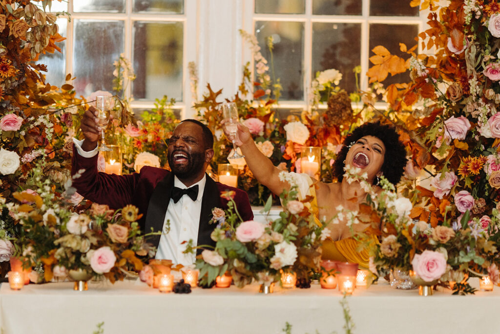Lush growing fall floral installation surrounds the couple at this autumnal wedding’s sweetheart table composed of roses, ranunculus, lisianthus, dried hydrangea, delphinium, copper beech, and fall foliage creating floral colors of dusty rose, burgundy, mauve, copper, terra cotta, and hints of lavender. Fall wedding in Downtown Nashville. Design by Rosemary & Finch Floral Design in Nashville, TN. 