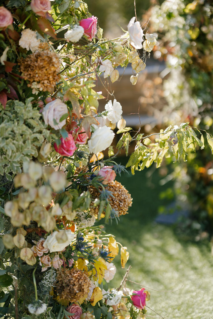 Broken Arch Ceremony Backdrop for fall Carolina’s wedding in Raleigh. Floral colors in mauve, cream, dusty pink, dusty blue, copper, and natural green. Floral accents of roses and fall color branches. Design by Rosemary and Finch Floral Design based out of Nashville, TN. 
