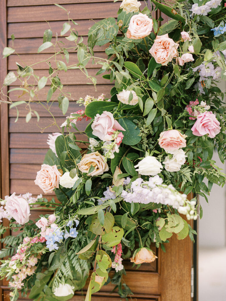 Gate and gatehouse tropical column floral installation for destination spring destination beach wedding in Exuma, Bahamas. Orchids and roses in tropical colors of orange, pink, lavender, dusty blue pale yellow and natural greens. Design by Rosemary & Finch Floral Design. 