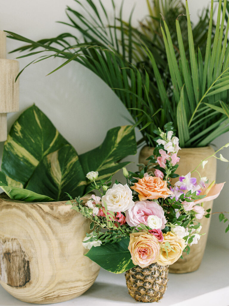 Tropical floral arrangements in pineapples for private estate spring destination beach wedding in Exuma, Bahamas. Orchids and roses in tropical colors of orange, pink, lavender, dusty blue pale yellow and natural greens. Destination floral design by Rosemary & Finch Floral Design.
