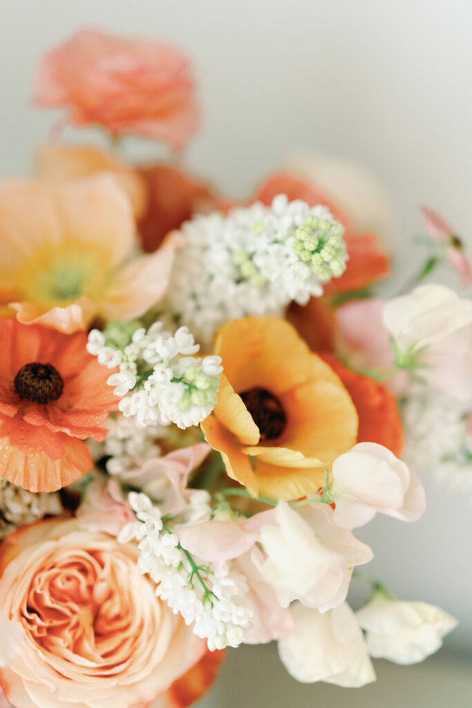Lush colorful bridal bouquet with flower colors in tangerine, peach, coral, blush, yellow, orange, and cream. Destination beach wedding bouquet with pops of pink and ranunculus, poppies, lilac, and rose flowers. Spring wedding shoot at The Ritz-Carlton Amelia Island. Destination floral design by Rosemary & Finch Floral Design. 
