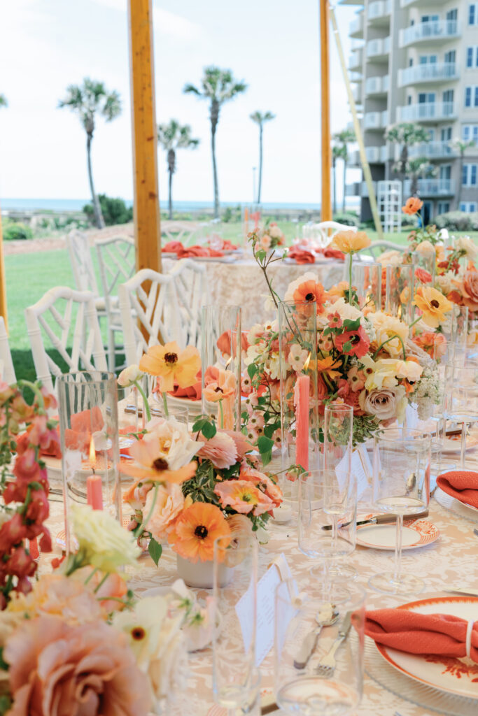 Colorful low centerpieces for beach wedding at The Ritz-Carlton Amelia Island. Wedding reception photoshoot with lush ranunculus, poppies, and dogwood branches. Fun tangerine, peach, blush, coral, orange, and cream floral colors for vibrant spring beach wedding reception. Fun colorful candles in pink and coral for spring wedding reception. Destination floral design by Rosemary & Finch Floral Design. 