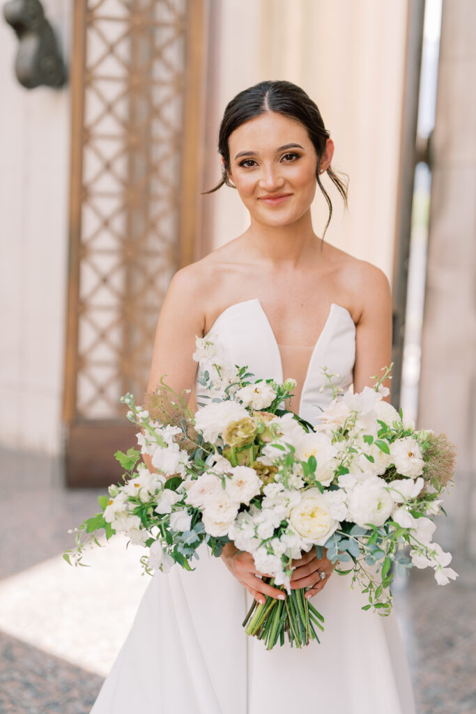 Whimsical bridal bouquet in cream, white, taupe, and champagne colors. This summer wedding bouquet is full of fun texture and represents elegant and timeless floral design. Composed of roses, lisianthus, smoke bush, ranunculus, and natural greenery. White and green floral wedding in downtown Nashville. Design by Rosemary & Finch Floral Design in Nashville, TN.