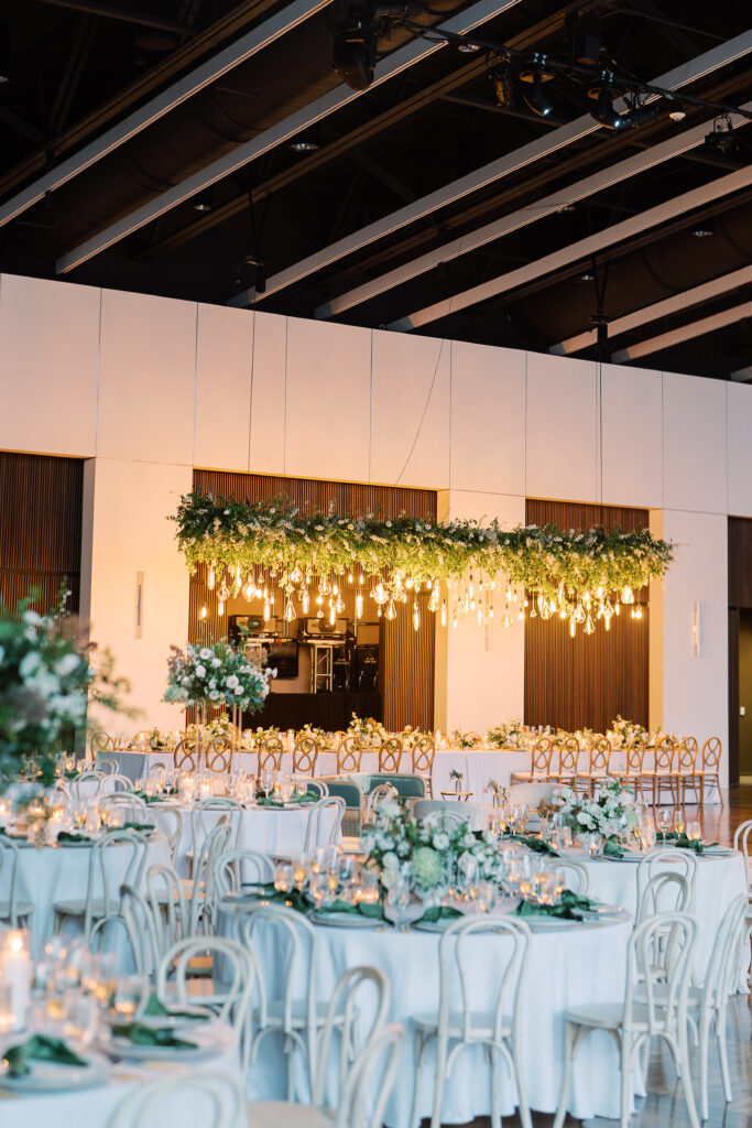 Epic floral installation for garden-inspired summer wedding. Large and lush floral install over head table for timeless wedding design. Vine-like greenery and florals accent this hanging Edison bulb installation. Downtown classic white and green wedding. Design by Rosemary & Finch Floral Design in Nashville, TN. 