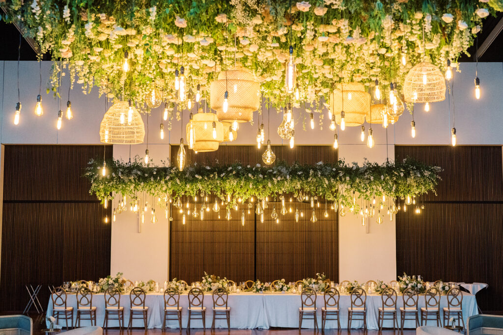 Large dance floor floral installation for classic summer wedding in downtown Nashville. Timeless floral design highlights this garden-inspired wedding reception. Hanging flowers and rattan chandeliers create lush floral dance floor moment. Classic white and green wedding with floral colors in cream, white, taupe, and champagne. Summer floral design full of roses, ranunculus, hydrangea, cosmos, and lisianthis. Design by Rosemary & Finch Floral Design. 