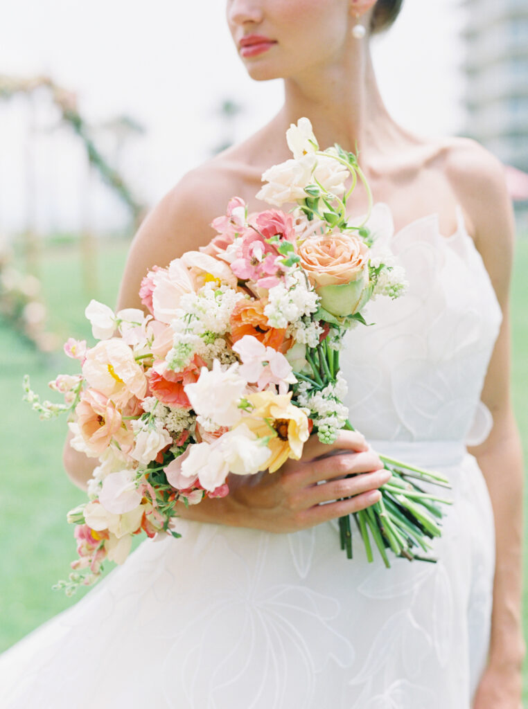 Lush colorful bridal bouquet with flower colors in tangerine, peach, coral, blush, yellow, orange, and cream. Destination beach wedding bouquet with pops of pink and ranunculus, poppies, lilac, and rose flowers. Spring wedding shoot at The Ritz-Carlton Amelia Island. Destination floral design by Rosemary & Finch Floral Design. 