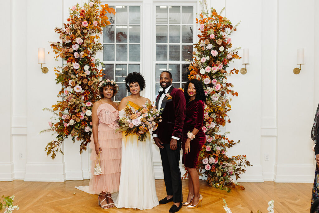 Artful asymmetrical floral fall wedding ceremony backdrop sets the autumnal colors of mauve, dusty rose, burgundy, terra cotta, and copper florals composed of roses, copper beech, delphinium, raintree pods, mums, and fall foliage. Fall wedding in Downtown Nashville. Design by Rosemary & Finch Floral Design in Nashville, TN. 