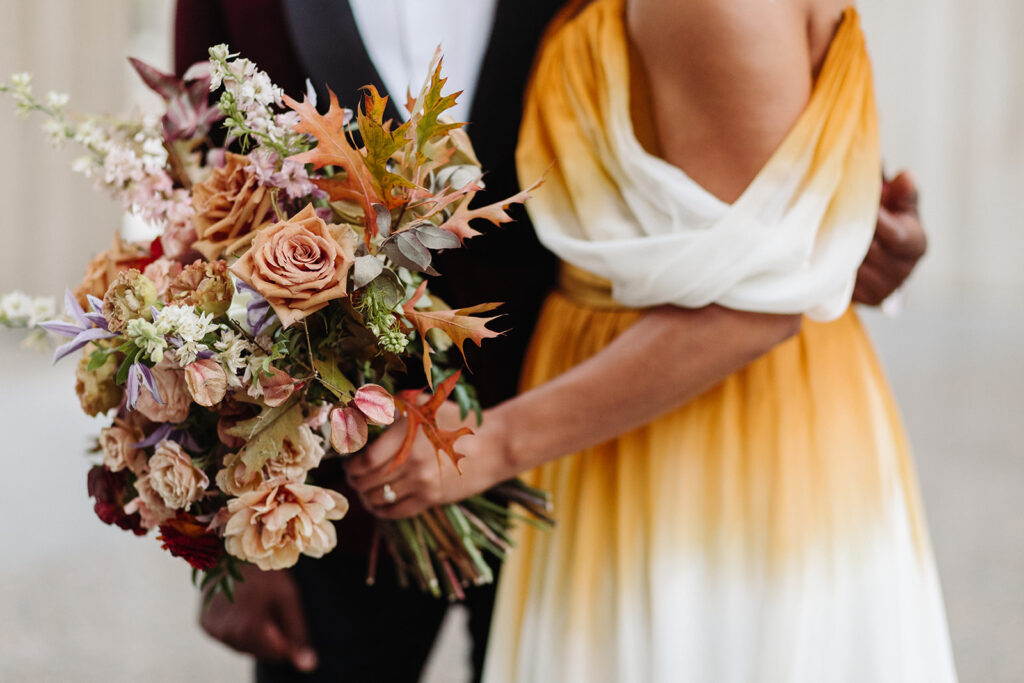 Autumnal bridal bouquet composed of roses, ranunculus, delphinium, clematis, lisianthus, and fall foliage floral hues of burnt orange, mauve, dusty rose, taupe, and lavender. Fall wedding in Downtown Nashville. Design by Rosemary & Finch Floral Design in Nashville, TN. 