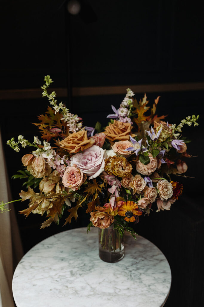 Autumnal bridal bouquet composed of roses, ranunculus, delphinium, clematis, lisianthus, and fall foliage floral hues of burnt orange, mauve, dusty rose, taupe, and lavender. Fall wedding in Downtown Nashville. Design by Rosemary & Finch Floral Design in Nashville, TN. 